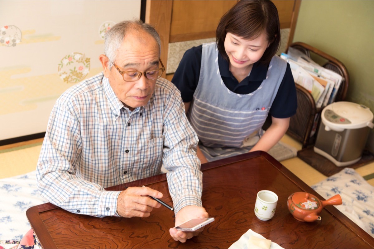 介護スタッフに教わりながらスマートフォンを使う高齢の男性